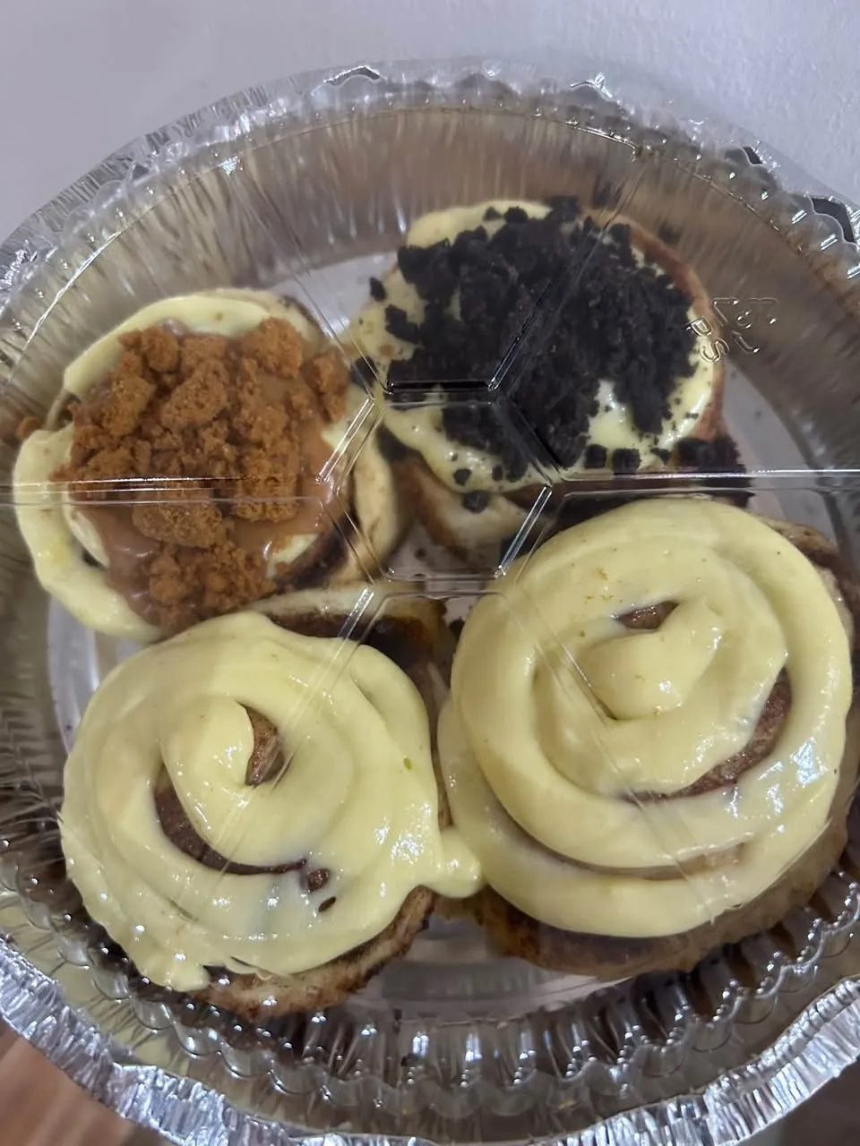Four cinnamon rolls with three different toppings in a round container, seen from above