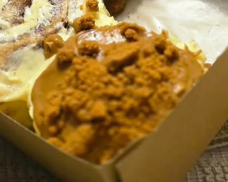 Close-up of a cinnamon roll topped with golden biscuit crumble and drizzle
